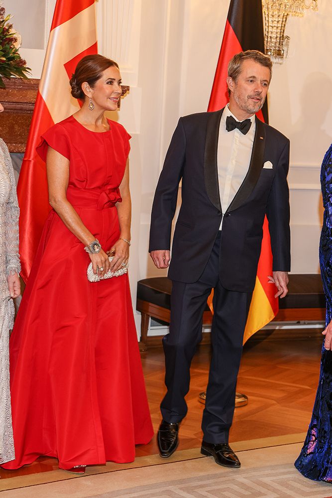 Queen Mary wears a red satin dress and silver jewelry. 