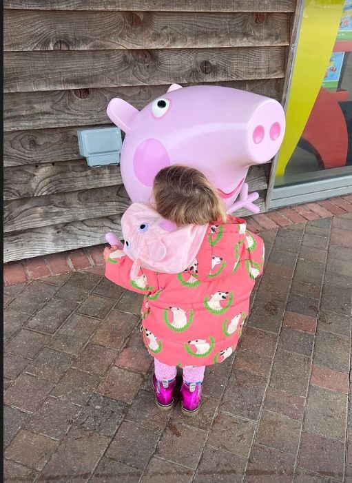 zA young girl hugging a statue of Peppa Pig