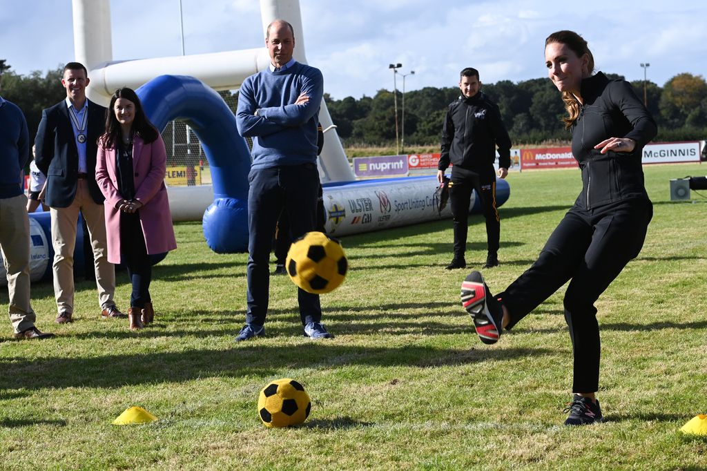 Princess Kate kicking a football while Prince William watches