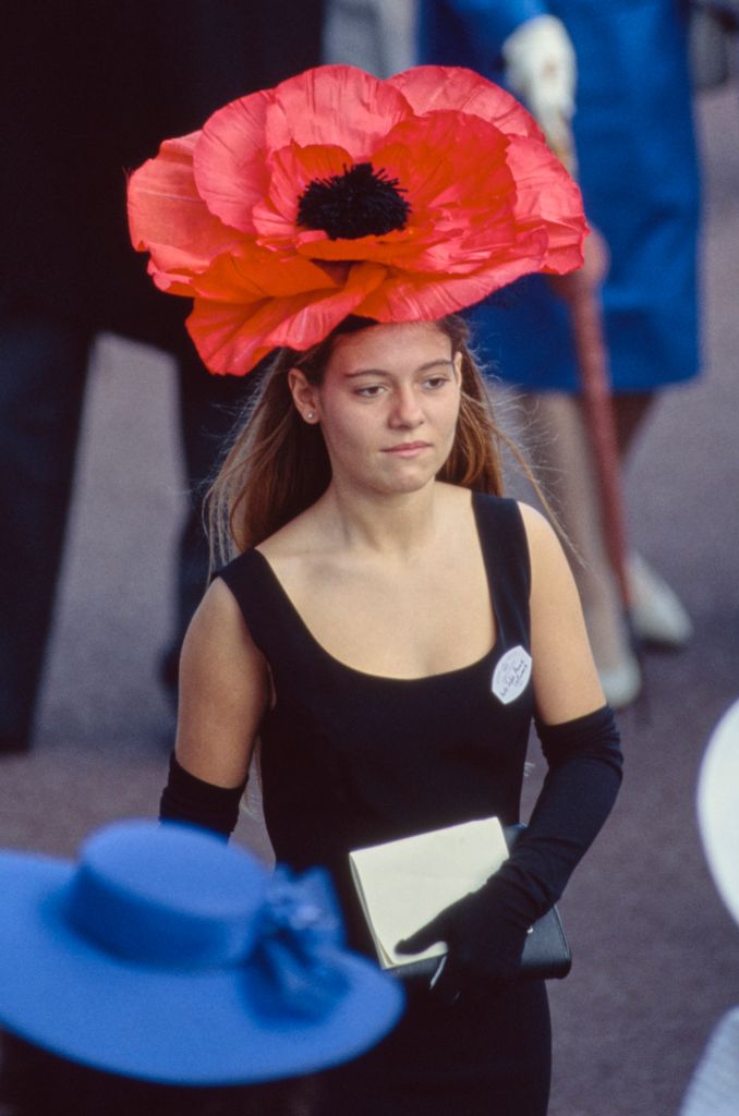 A female racegoer wearing a black dress, black evening gloves, and a red poppy hat on the first day of the Royal Ascot, 19 June 1990.