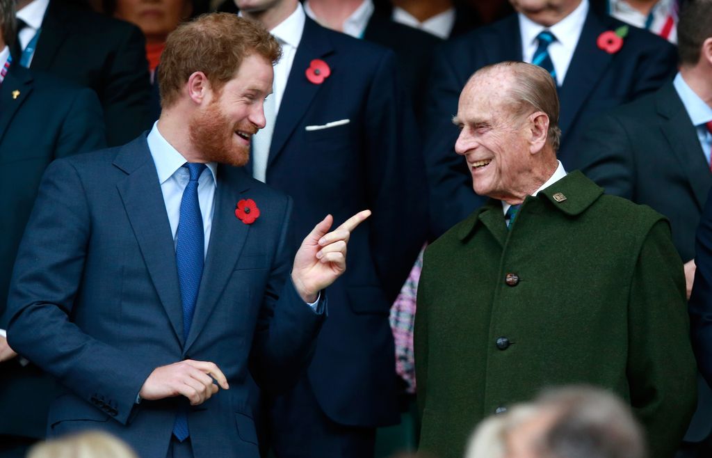 Prince Harry pointing and smiling at Prince Phillip dressed in a green coat