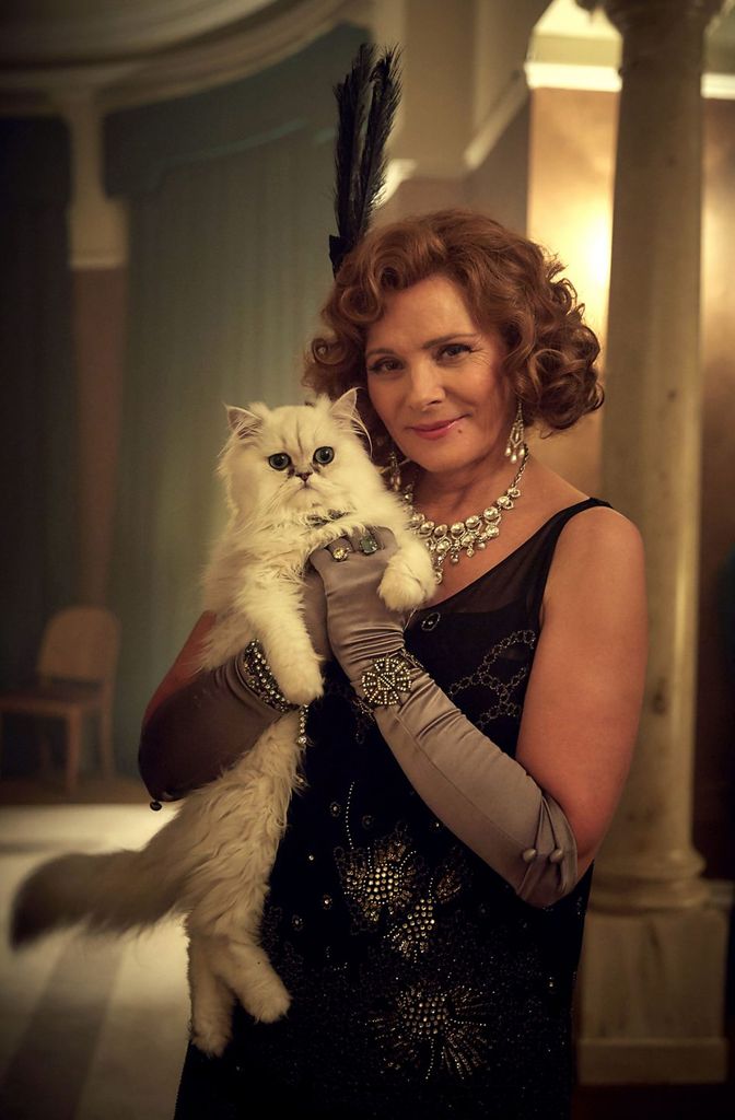 A woman in 1920s dress holds a white cat