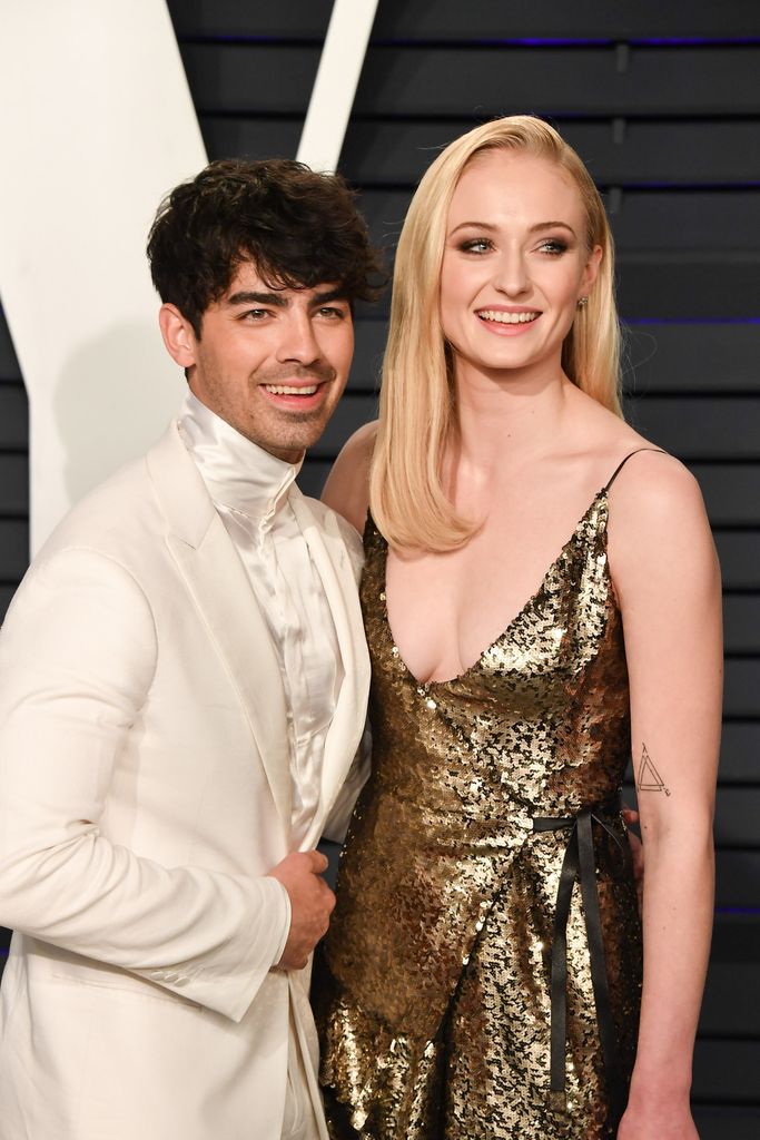 Joe Jonas in white suit with Sophie Turner in gold dress at 2019 Vanity Fair Oscar Party