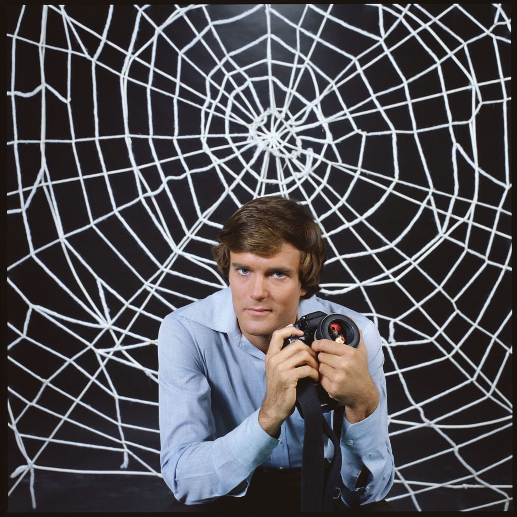 Promotional portrait of American actor Nicholas Hammond, as Peter Parker (whose secret identity is as the costumed superhero Spider-man), as he holds a camera and sits in front a large 'web' for the CBS television series 'The Amazing Spider-Man,' 1978. The series was based on a long-running comic book, developed by Stan Lee and Steve Ditko.