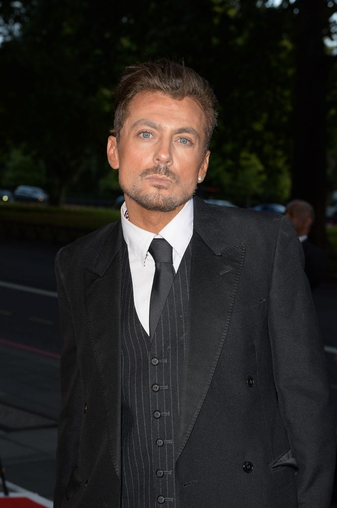 Paul Danan with a blank expression in a black suit