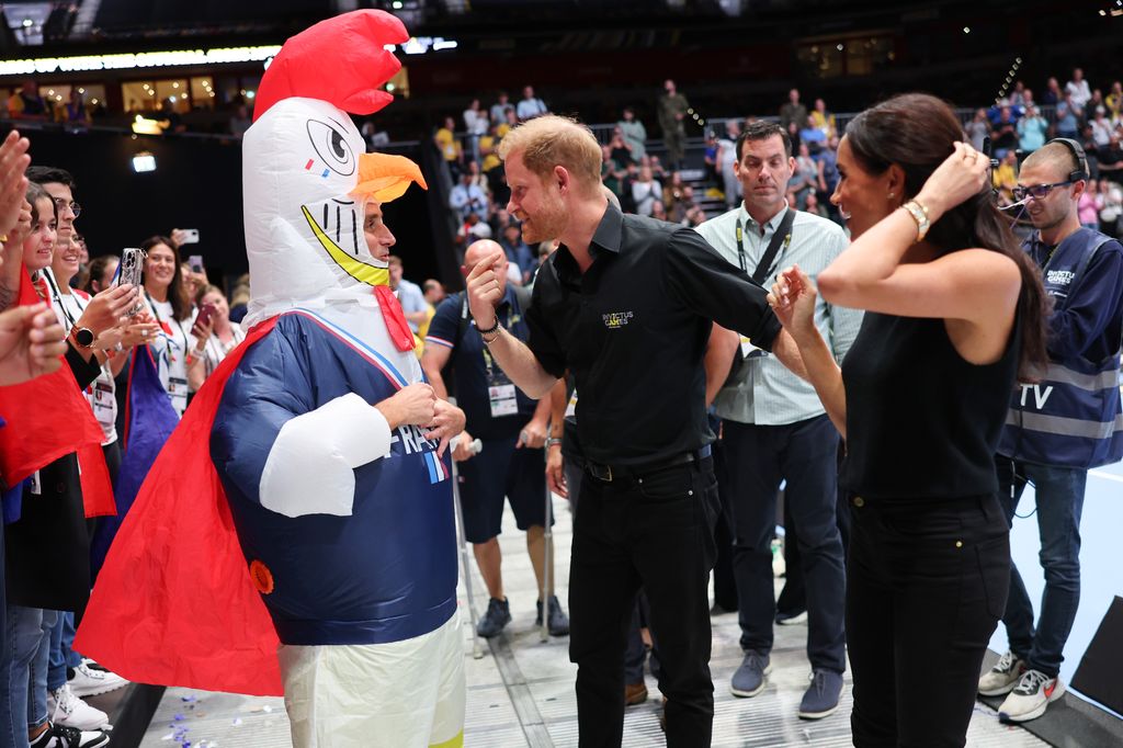 Prince Harry and Meghan Markle talking to a mascot in a chicken costume