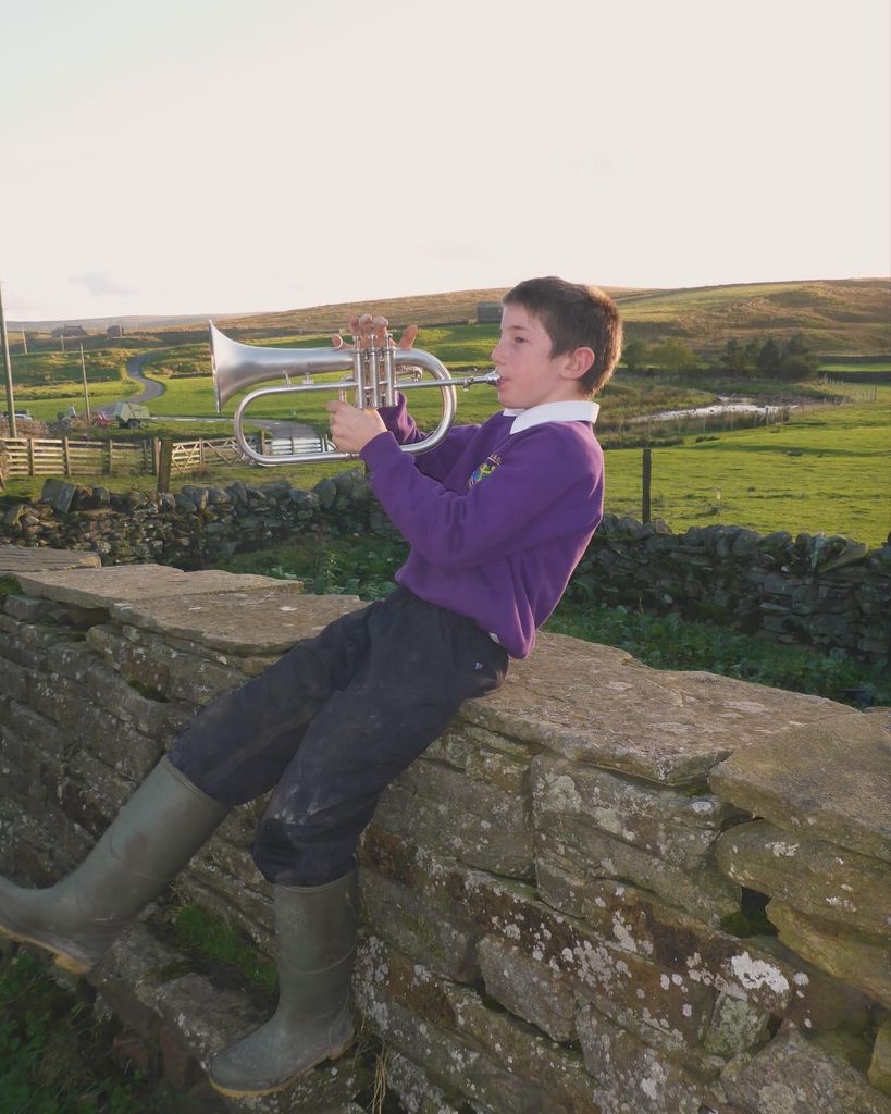 photo of boy playing musical instrument on stone wall 