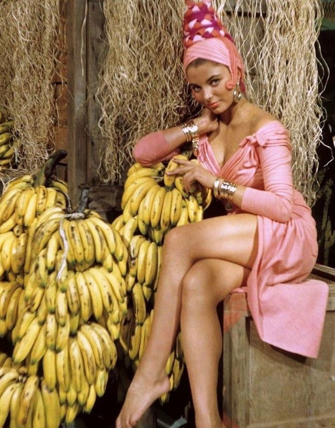 Joan Collins in still from The Opposite Sex (1956) in pink mini dress with several bunches of bananas