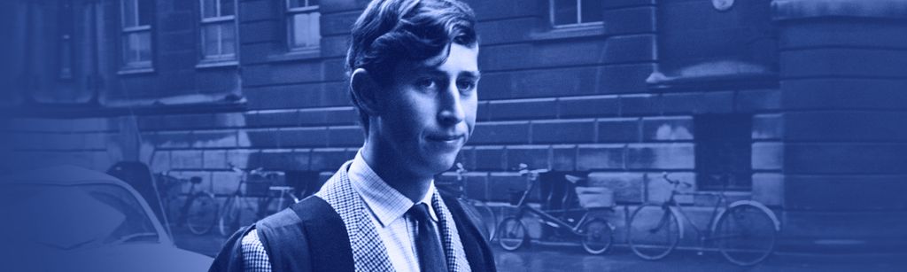 Young King Charles III wearing university robes over a tweed suit