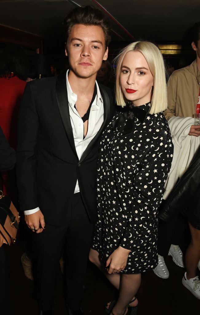 Harry Styles (L) wears a suit with his arm around his sister, Gemma Styles, who is dressed in a black and white patterned dress with tights.