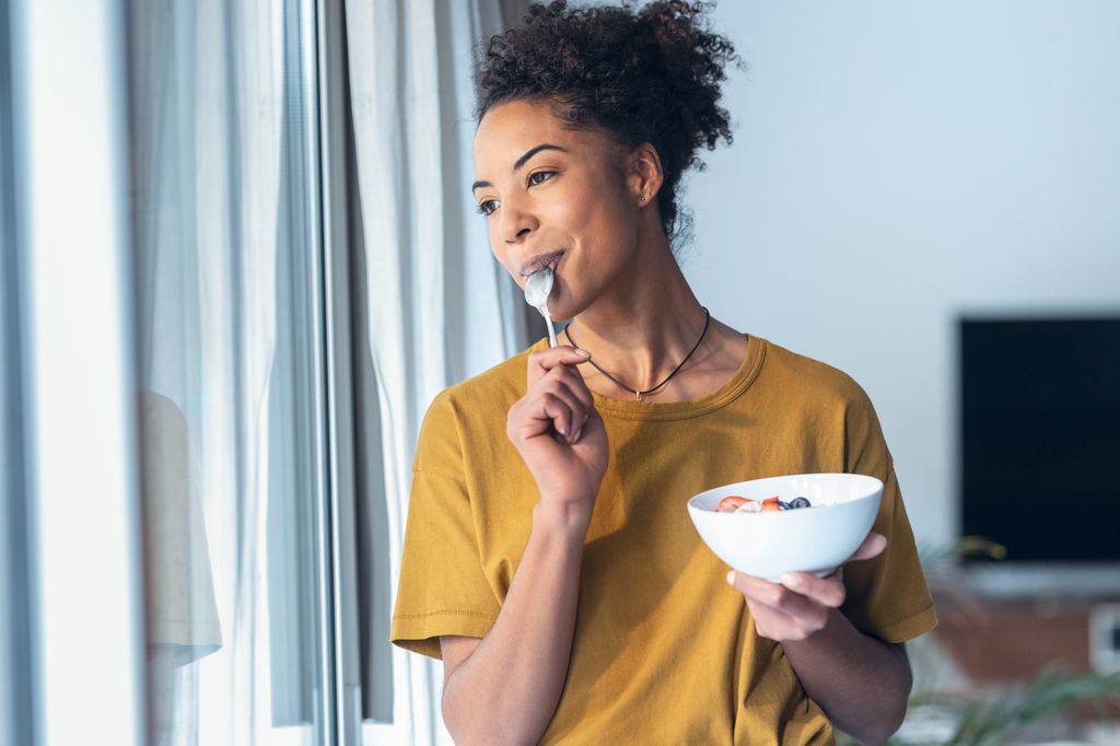 Woman in a yellow top smiling as she eats from a bowl