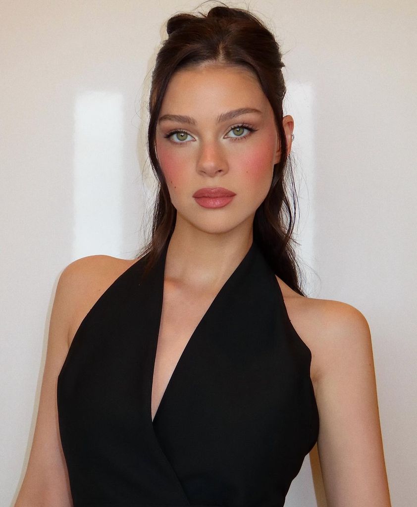 Nicola Peltz wearing a black halterneck top with her hair half-up half-down and a make up look featuring romantic rosy cheeks