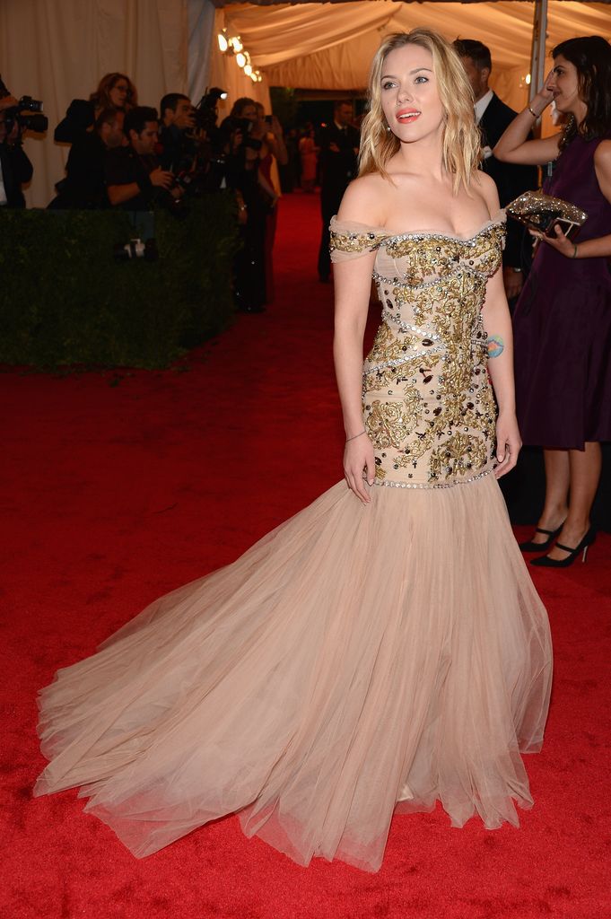 Scarlett Johansson stuns at the 2012 Met Gala in a gold-embellished off-the-shoulder Dolce & Gabbana gown with a voluminous nude tulle skirt, striking a balance between Old Hollywood glamour and fairytale princess fantasy.