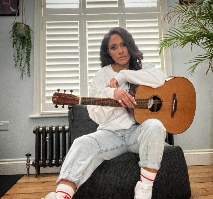 Alex Scott in a living room holding a guitar