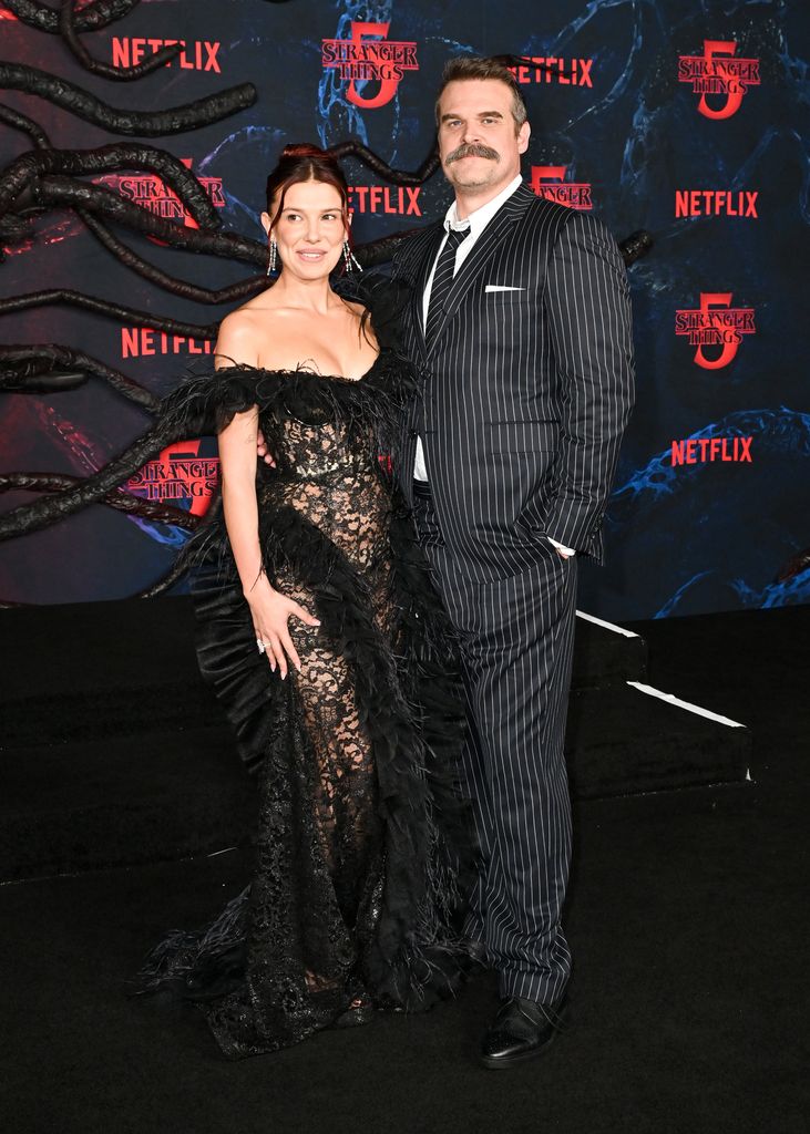 Millie Bobby Brown in black lace dress and David Harbour in pinstripe suit