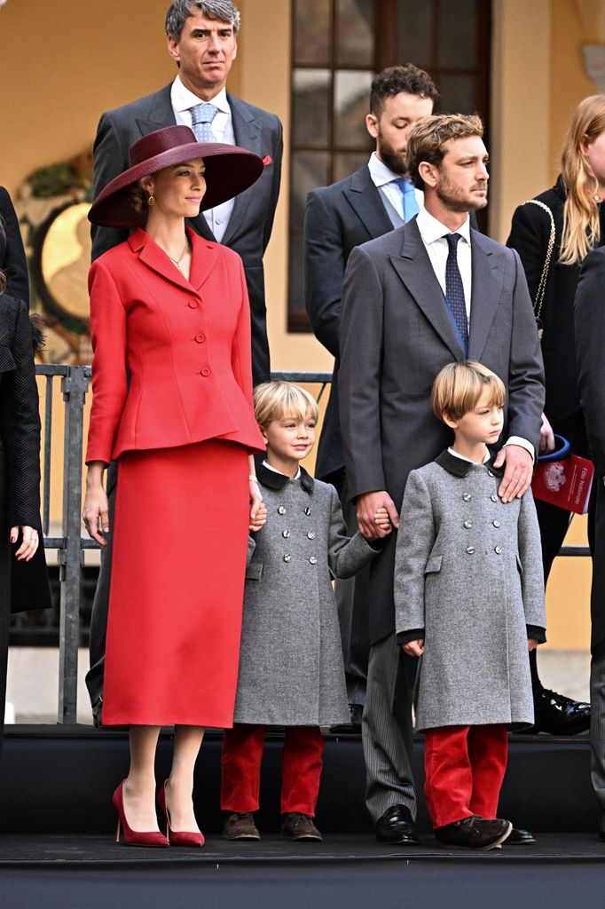 Beatrice Borromeo stands with her family in a red structured suit and matching wide-brim hat, coordinating with her sons' red velvet trousers.