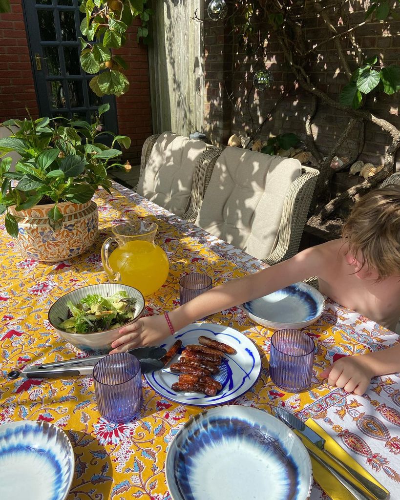 A young boy reaching for a plate of food on a vibrant yellow tablecloth