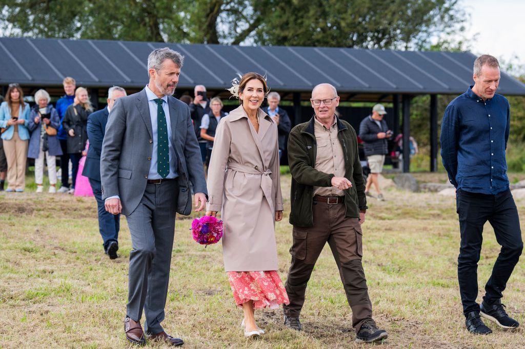 King Frederik X and Queen Mary walking on grass with two men