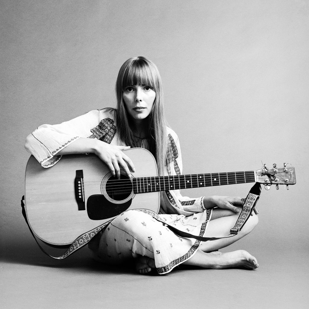 Portrait of American musician Joni Mitchell seated on the floor with her acoustic guitar in her lap.  This image was from a shoot for the fashion magazine Vogue.  Mitchell wears a white cotton dress.  (Photo by Jack Robinson/Hulton Archive/Getty Images)
