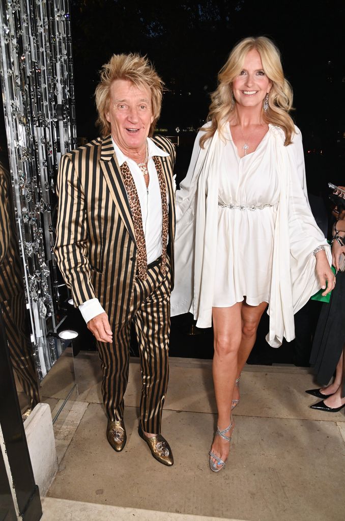 Rod Stewart with spiky hairdo in gold and black striped suit and shirt leaving Annabels with wife Penny Lancaster in white dress