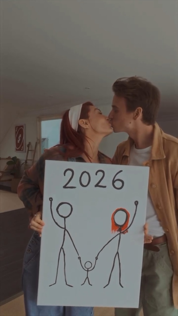 Two people kiss while holding up a drawing