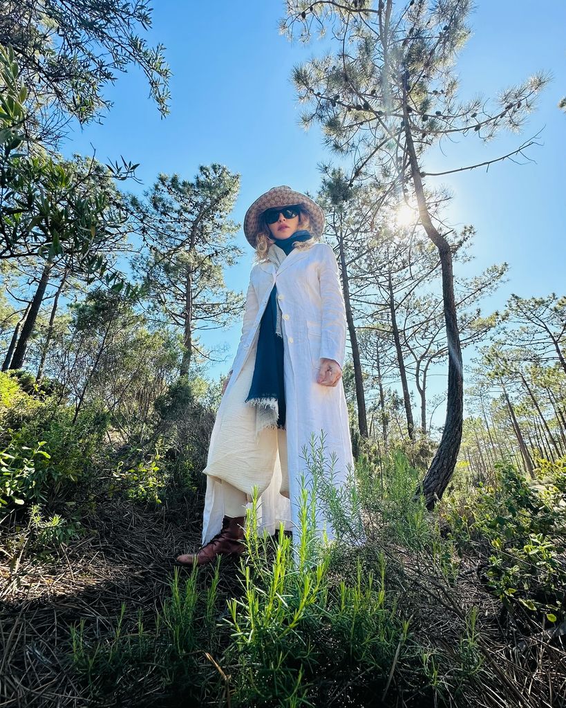 Madonna wearing a white jacket, large hat and sunglasses, standing in a field