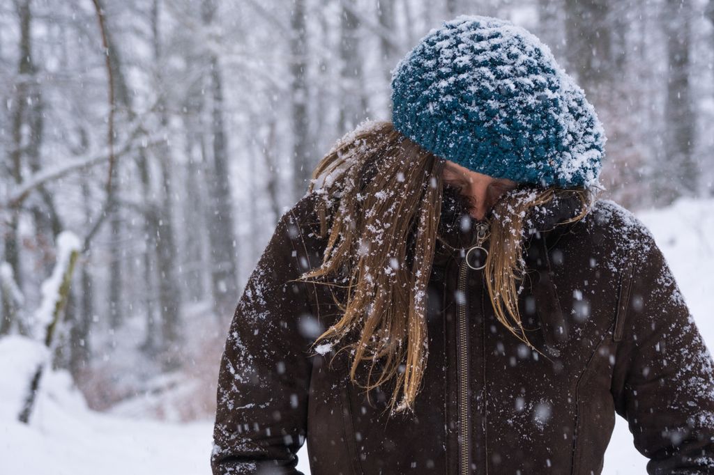 A woman in the snow with her coat zipped up over her face 