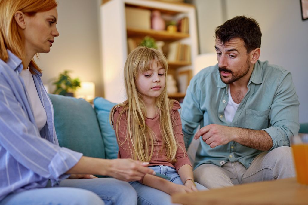 Parents sitting on the sofa in the living room, discussing their daughter's recent mistake while she listens with a sad expression. Tension fills the air as they address her behavior