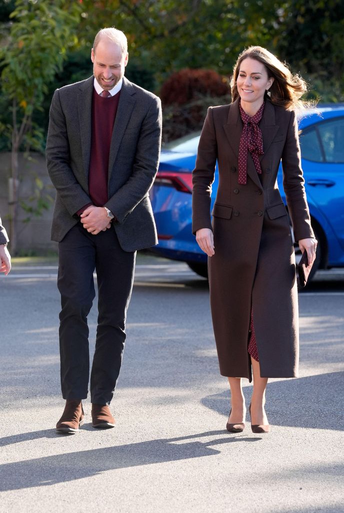 The Prince and Princess of Wales in brown coat walking