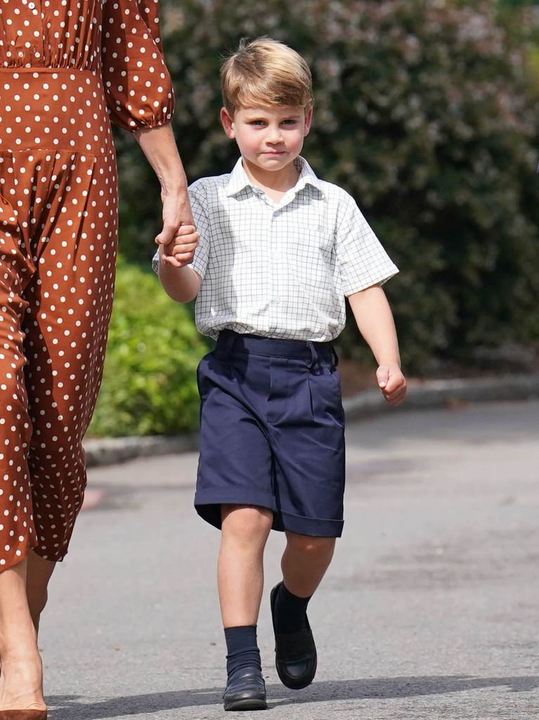 Le prince Louis marche main dans la main avec sa mère en short bleu et chemise à manches courtes.