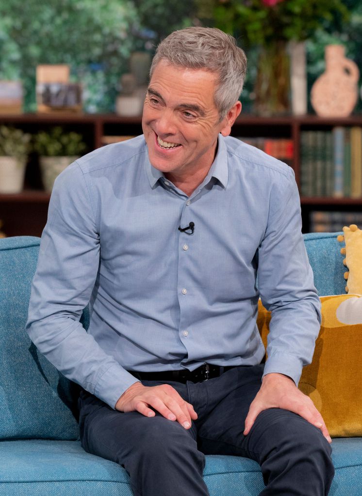 James Nesbitt sitting on s sofa in a blue shirt and trousers