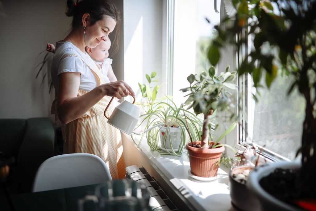woman holding baby and watering plants 