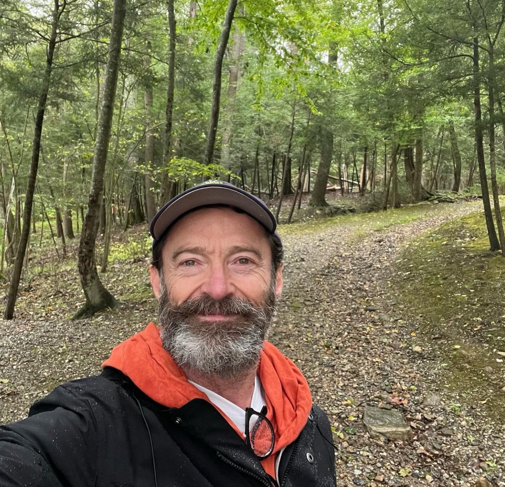 Photo posted by Hugh Jackman on Instagram September 24, 2023 where he is smiling while on a hike through a forest.