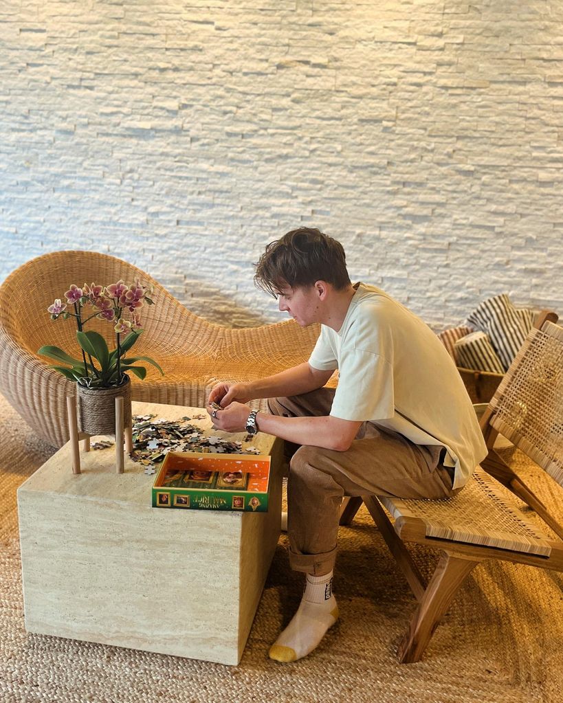 Joe Sugg sits on a rattan chair and does a puzzle