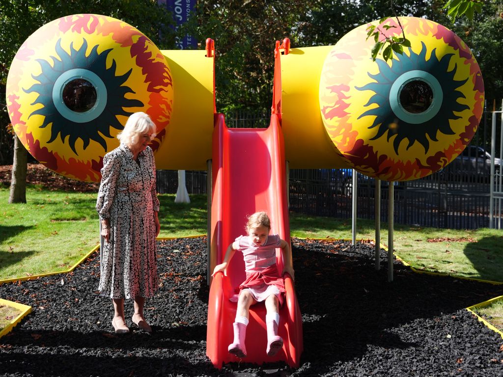Queen Camilla observing a child slide down a slide