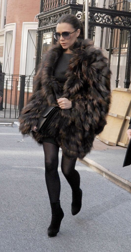 Victoria Beckham wears a fluffy brown coat, black mini skirt, tights and heels paired with sunglasses and a black leather bag over her shoulder. 