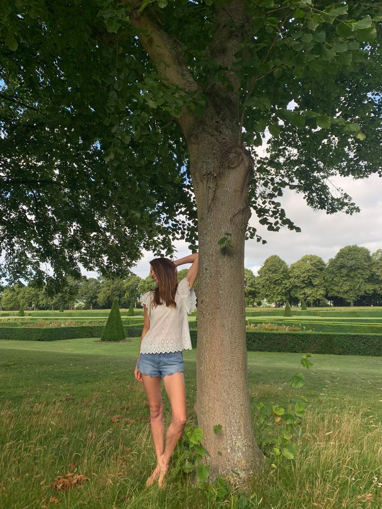 Woman standing against a tree in short denim shorts and no shoes