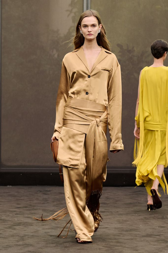 A model wears a caramel coloured silk top and wide leg trousers with a knotted cummerbund worn over the trousers