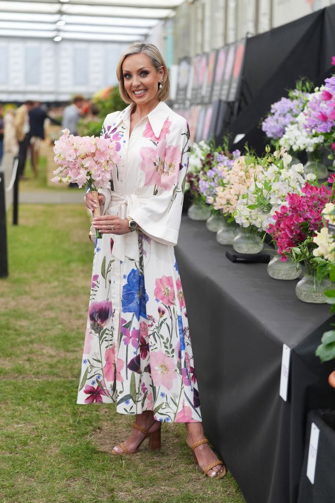 Amy Dowden in a white shirt dress printed with colourful florals poses holding a bouquet at the Chelsea Flower Show 2025.