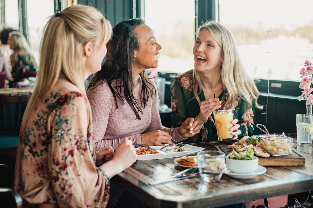 A front view shot of three beautiful mid-adult women enjoying brunch together in a restaurant, they are sitting around a table and laughing with eachother.