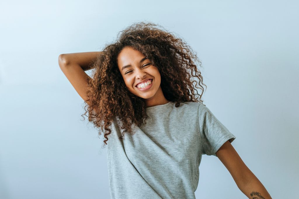 Portrait of woman with afro hair smiling with white wall background.