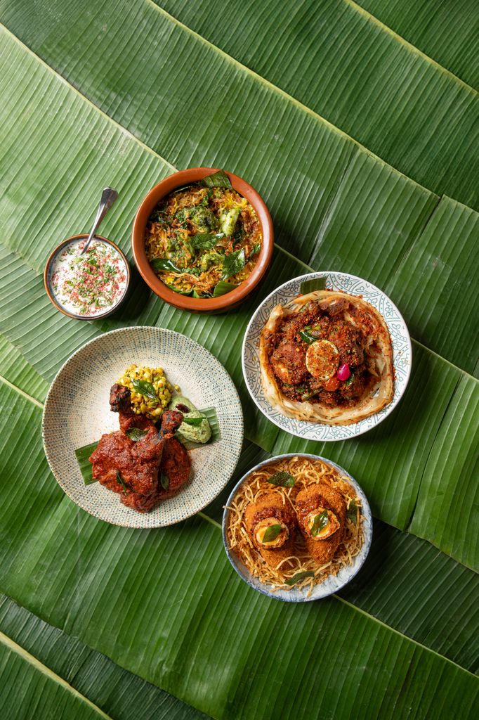 five indian dishes on plates with palm leaves behind