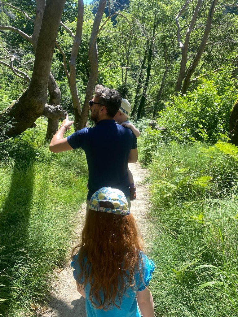 Man carrying toddler on a wooded path with girl just behind