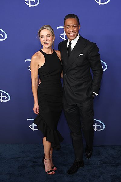 Amy Robach in a black dress with TH Holmes wrapping arm around her