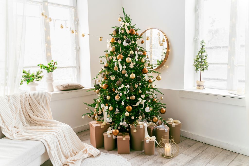 White and spacious domestic living room decorated with Christmas fir tree and pastel holiday decor. Festive craft gift boxes and wrapped presents for family and friends