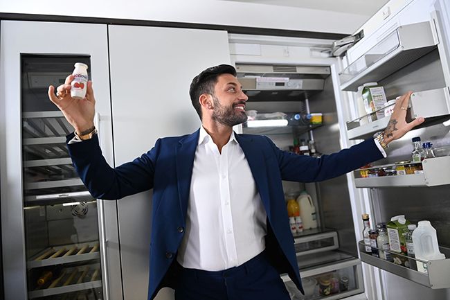 Giovanni Pernice holding Actimel bottle in front of open fridge