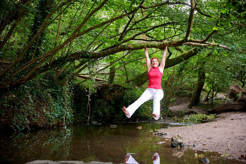 woman swinging from a tree in a pink top and white jeans