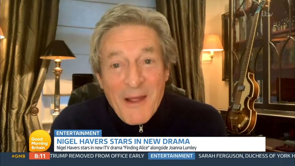 Nigel Havers sitting in a room with a guitar in the background