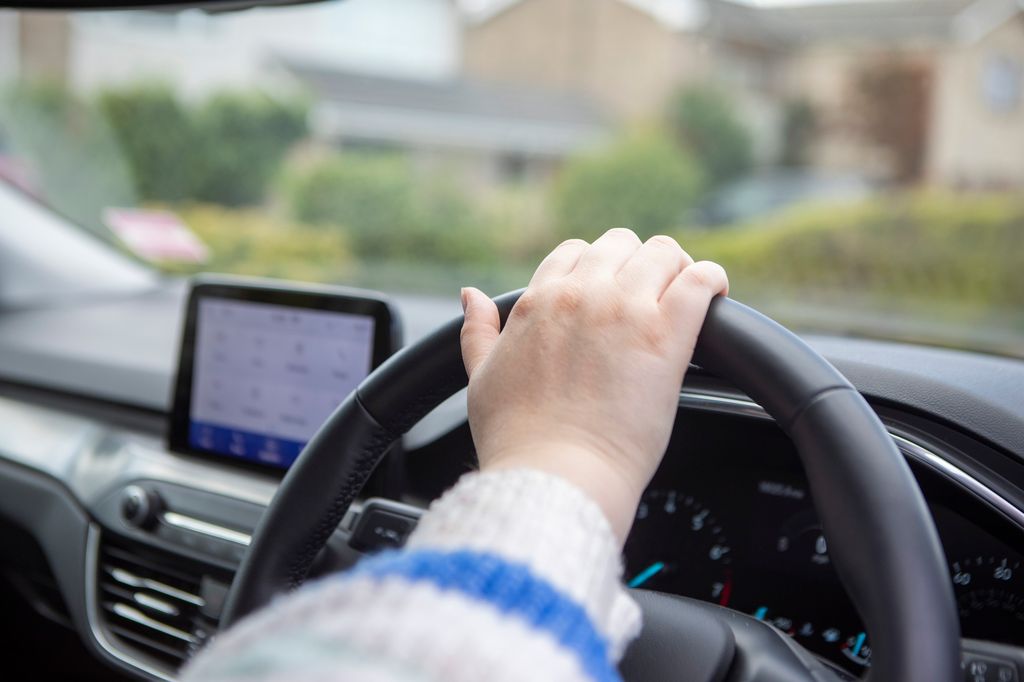 Close-up of a woman's hand on a car steering wheel before starting a car journey