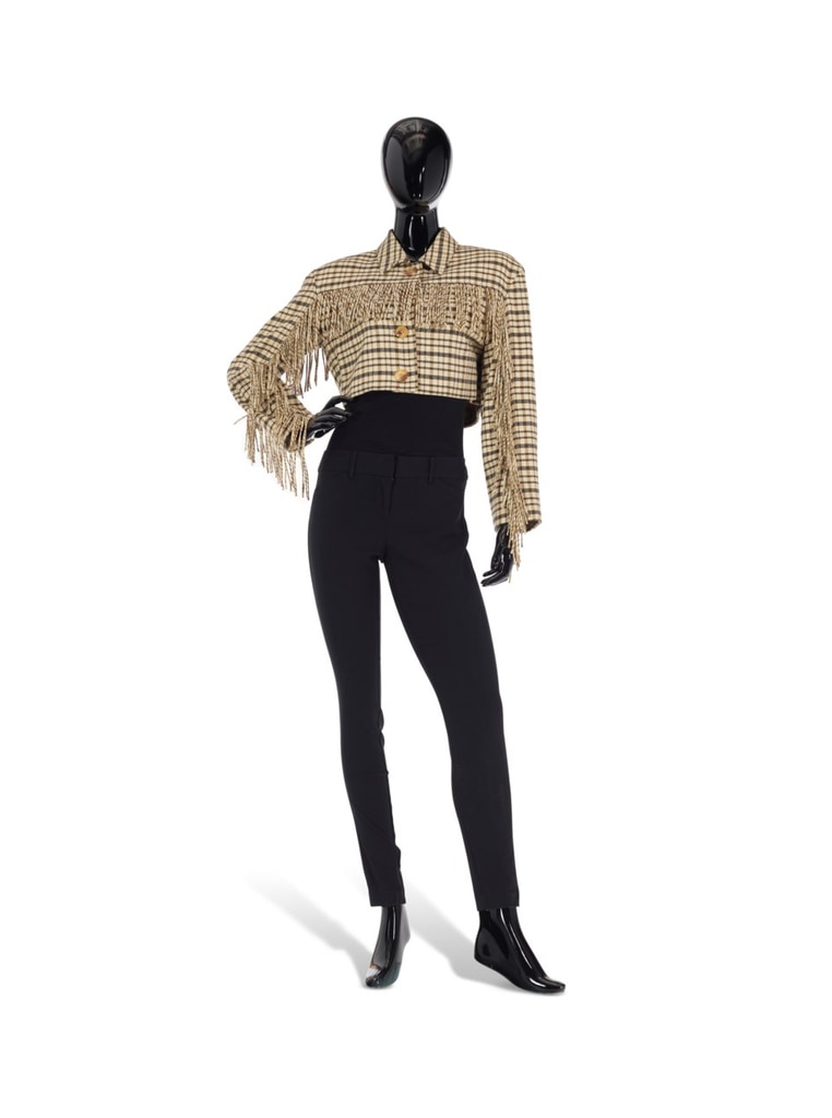  A cropped, beige and black plaid jacket with fringe by Perry Ellis (Late 20th/Early 21st Century). The jacket is worn over a black top and paired with black pants, creating a chic, edgy silhouette. The mannequin strikes a confident pose. This striking piece was part of Iris Apfel's personal collection.